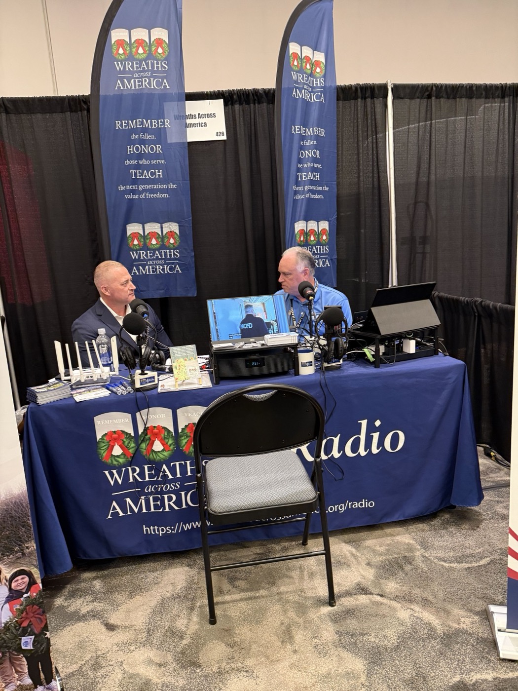 Two hosts recording a live radio segment at the Wreaths Across America booth